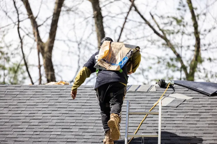 Senco roofer carrying a bundle of shingles up an asphalt shingle roof
