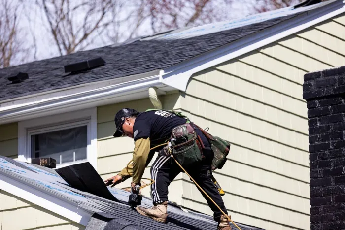 Senco roofer in company gear fastening new asphalt shingle courses on a home near Tewksbury, MA