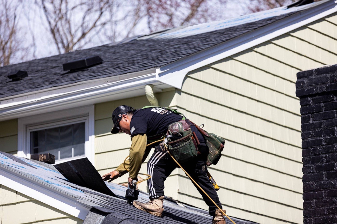 Senco roofer in company gear fastening new asphalt shingle courses on a home near Tewksbury, MA
