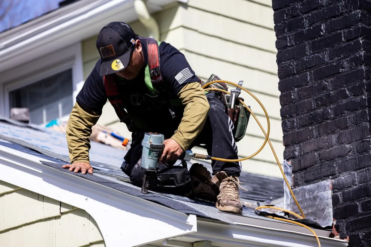 Senco roofer detailing shingle courses beside a brick chimney on a Massachusetts home
