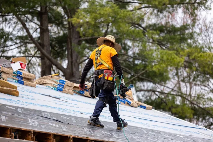 Senco roofer walking across new underlayment during a spring roof replacement, with trees leafing out behind him